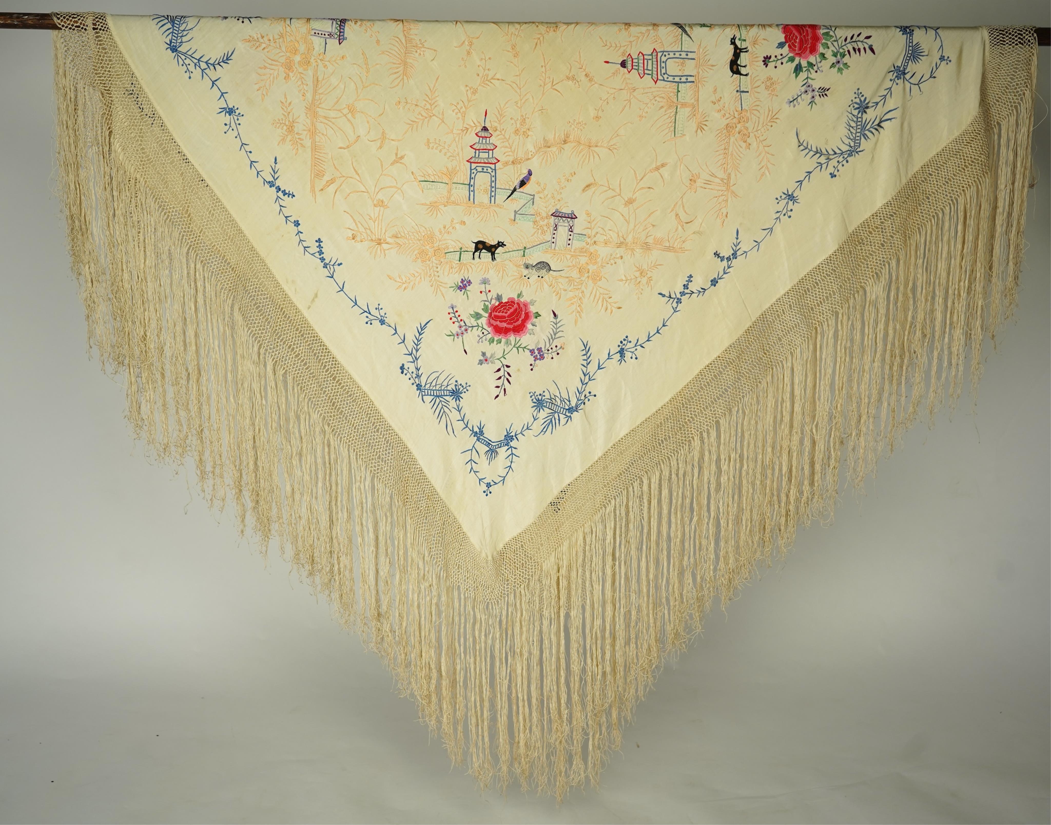 A Chinese cream silk polychrome embroidered shawl with a long fringe. Embroidered with four unusual corner cartouches of Pagoda, flowers, birds, cats and dogs. 132cm x 126cm.